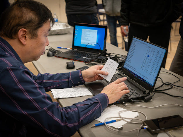 A person sitting at a table with a computer and a piece of paper

Description automatically generated