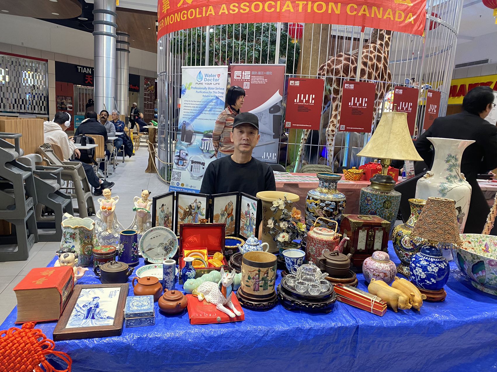 A person sitting behind a table with various objects on it

Description automatically generated