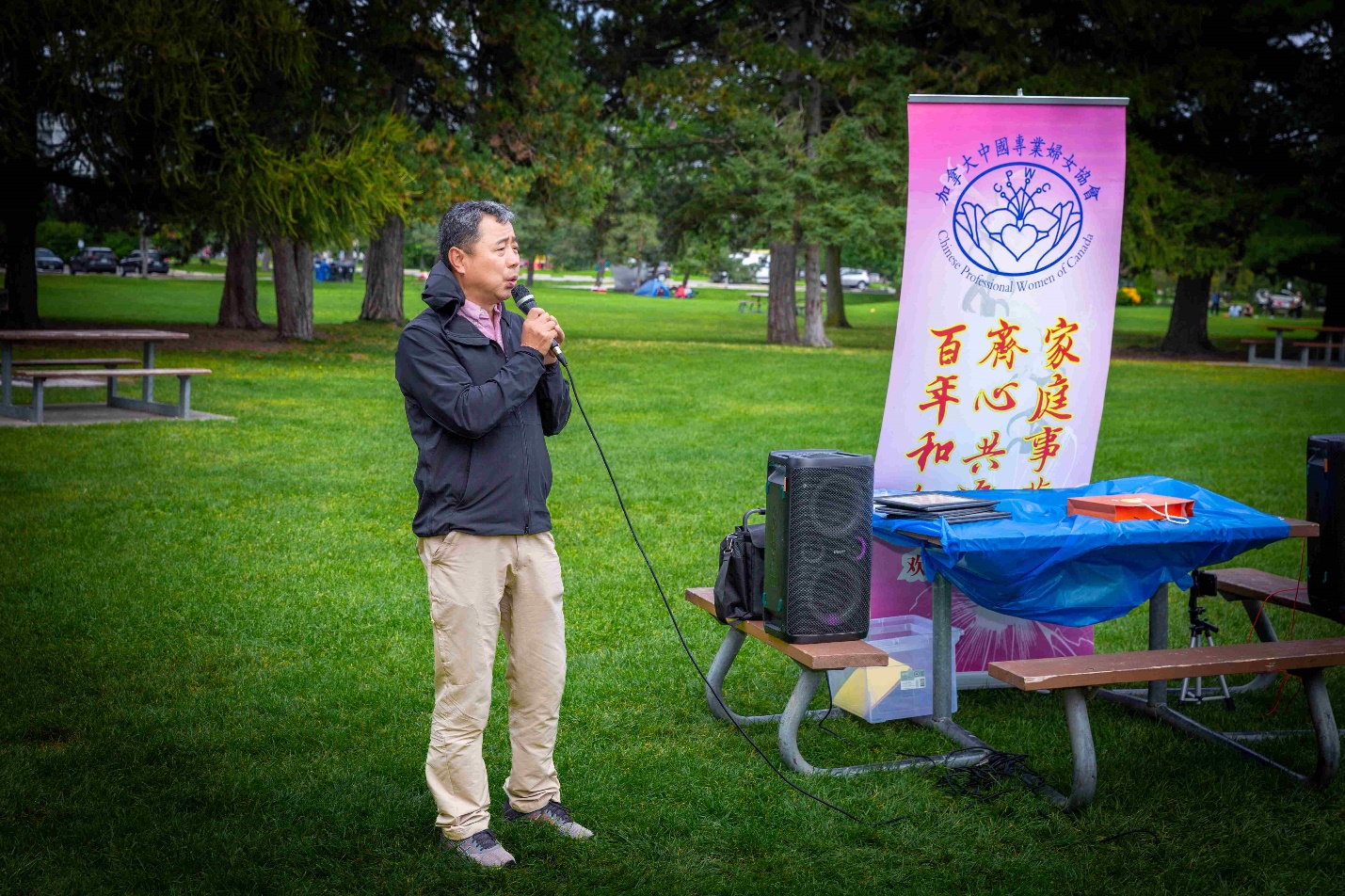 A person holding a microphone in front of a picnic table Description automatically generated