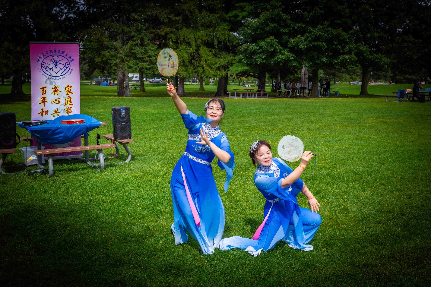 Two women in blue dresses dancing in a park Description automatically generated