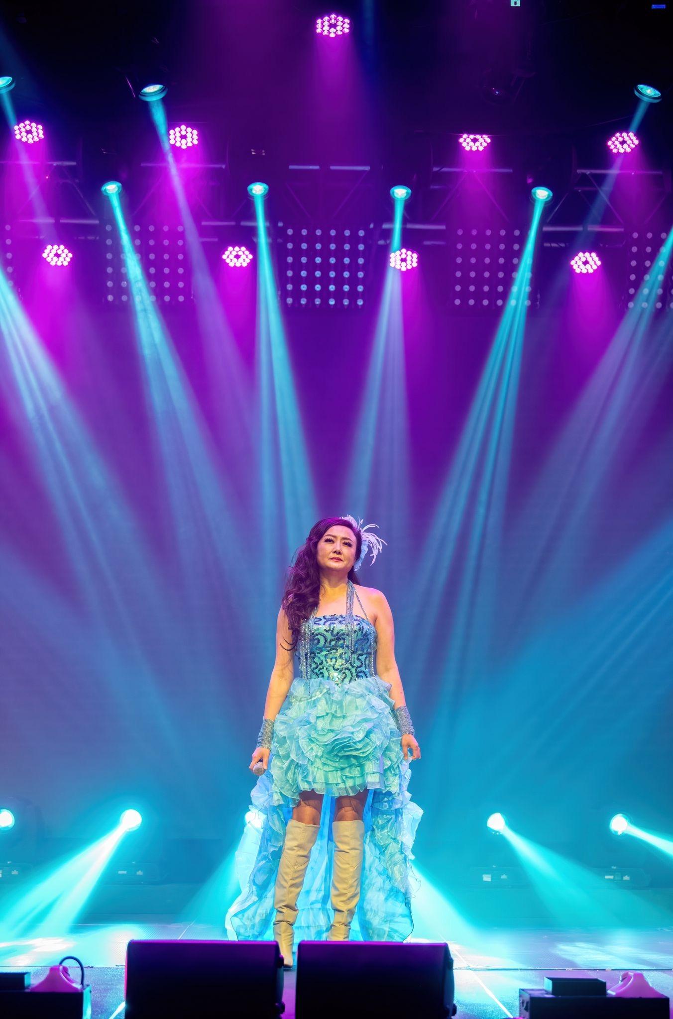 A person in a blue dress on a stage with lights

Description automatically generated